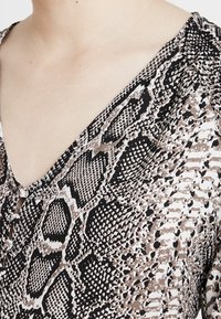 Blusa leggera a scollo a V in un motivo a stampa serpente nero, bianco e marrone, con dettaglio a bottone sul colletto e texture morbida.