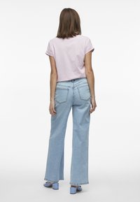 Camisa de manga corta rosa claro con puños doblados, combinada con pantalones vaqueros de pierna ancha de cintura alta en azul claro y zapatos de tacón bloque azul.