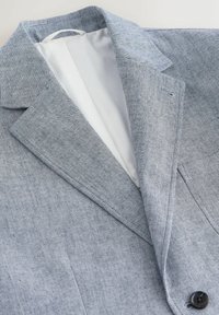 Veste texturée gris clair avec col à revers cranté, fermeture à un bouton, et doublure intérieure blanche posée à plat.