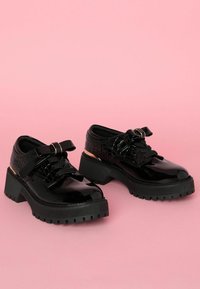 Scarpe con piattaforma in vernice nera, caratterizzate da un motivo in pelle di coccodrillo testurizzato, con design allacciato, un accento a fiocco e suola in gomma spessa.