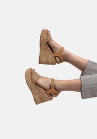 Sandali con zeppa beige, dotati di una piattaforma in sughero, design open-toe e dettagli intrecciati, fissati con un cinturino alla caviglia regolabile.