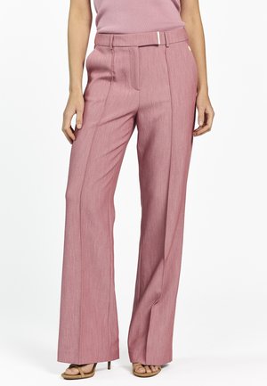 Vrouw met een hooggesneden, wijd uitlopende broek in rozenroze met een bijpassende riem, gecombineerd met beige open-toe sandalen met hak.