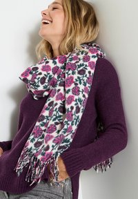 Bufanda con un patrón floral que presenta una base blanca con flores en tonos rosa y verde oscuro, material suave y flecos de colores variados.