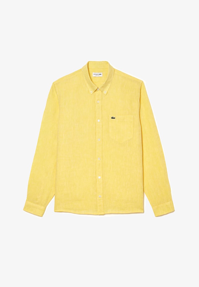 Chemise à manches longues jaune à boutons, en tissu texturé. Elle possède une poche poitrine unique et un petit logo Lacoste sur le côté gauche.