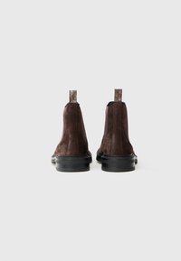 Stivali ankle in suede marrone con suole in gomma nera. Presentano un pannello sul tallone testurizzato e pannelli laterali elasticizzati per una facile calzata.