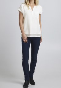 Kremowa bluzka krótki rękaw z dekoltem w kształcie litery V i kieszonką, w połączeniu z granatowymi spodniami slim fit i czarnymi botkami za kostkę. Gładka struktura materiału.