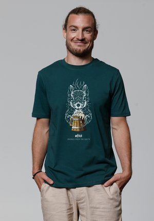 Teal cotton t-shirt with a squirrel graphic holding a beer mug, featuring white and gold details. Short sleeves, crew neck design.