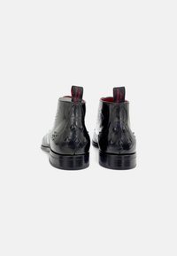Botas de tobillo de cuero negro con un acabado brillante, costuras detalladas, acentos en forma de diamante en los tacones y un interior rojo en contraste.