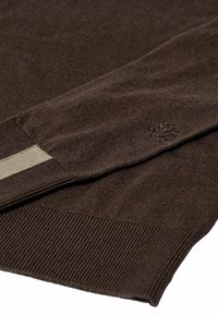 Rudas megztinis su gyslomis ant rankovių ir apačios, su šviesiai rudomis juostelėmis ir mažai logotipu šalia rankovės. Minkšta tekstūra ir prigludęs dizainas.