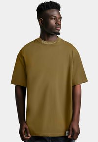 T-shirt oversized di colore verde oliva realizzato in tessuto morbido, con scollatura rotonda e maniche corte, decorato con logo ricamato vicino al collo.