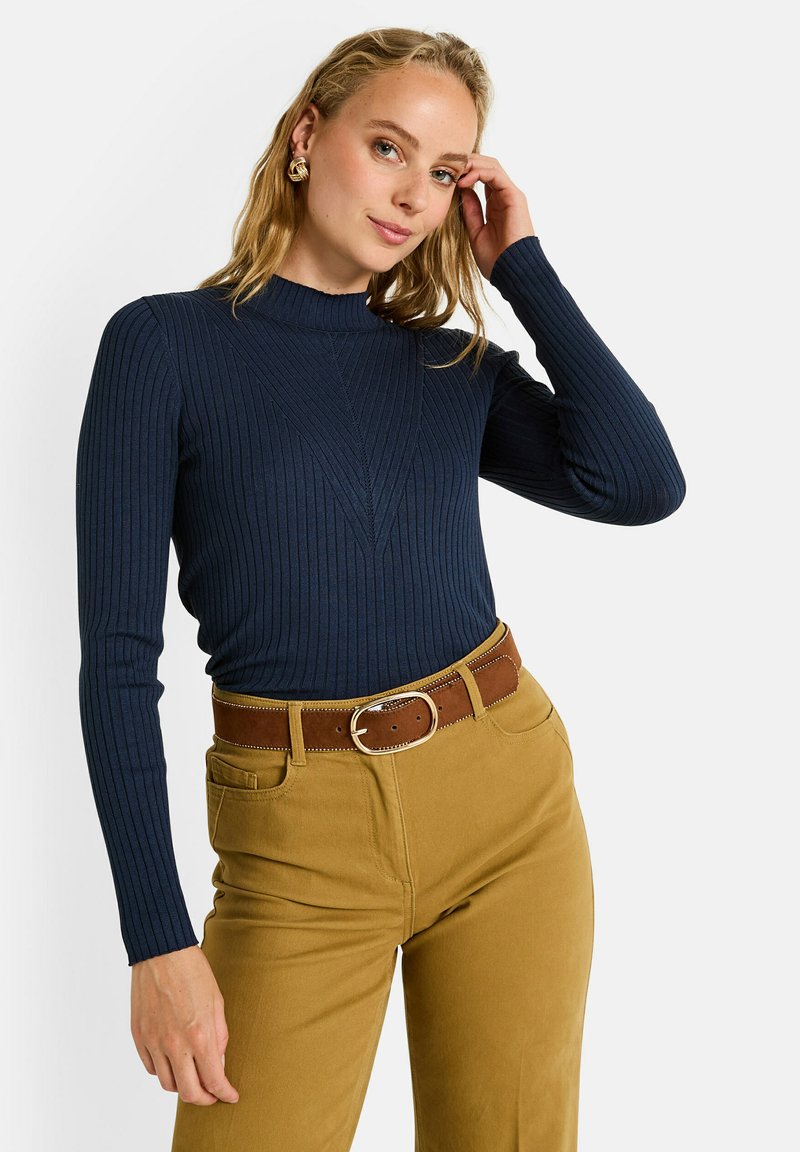 Col roulé côtelé bleu marine avec texture verticale, associé à un pantalon taille haute marron doré et une ceinture brune avec une boucle en argent.