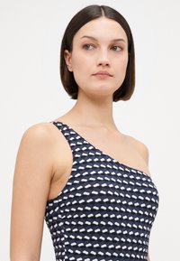 Robe asymétrique bleu marine présentant un motif texturé de formes blanches alternées, avec une bretelle unique et une coupe ajustée.