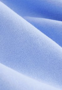 Tissu bleu clair avec une texture lisse, présentant un design à mailles fines et une légère élasticité, créant des plis et des drapés doux.