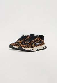 Sneakers med leopardmønster og svarte detaljer, gummisåler, teksturert stoff, og logo på tungen. Har tykke lisser og en polstret design.