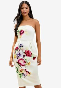 Mouwloze bloemenjurk van crème stof, met levendige roze, paarse en gele bloemen. Getailleerd ontwerp met een knielange silhouet.