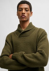 Suéter de punto con una apariencia gruesa y texturizada en verde oliva, con un cuello doblado y puños acanalados. Corte largo y relajado.