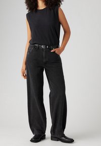 Svart ärmlös topp, högmidjade mörkgrå vida jeans, svart bälte och svarta ankelstövlar. Slät tyg med avslappnad passform.