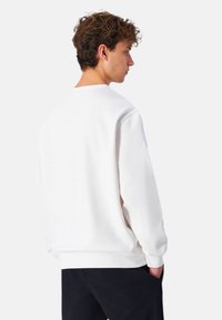 Sudadera de algodón blanca con mangas largas, puños de canalé y escote tipo crew. Textura suave, corte relajado con vista trasera.