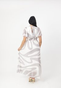 Robes longues grises et blanches à motifs avec des manches flutter, une taille cintrée et un dos en trou de serrure, associées à des talons ouverts.