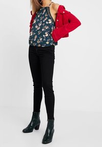 Blommönstrad mörk teal halterneck-topp, röd kordjacka, svarta skinny jeans och gröna texturerade ankelstövlar med klack.