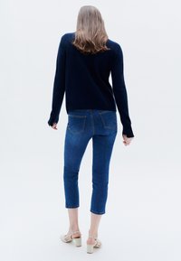 Navy Pullover mit langen Ärmeln und leicht lockerer Passform, kombiniert mit blauen Slim-Fit-Jeans. Beigefarbene High-Heels vervollständigen das Outfit.