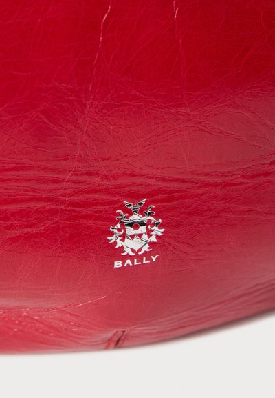 Sac en cuir rouge avec une finition texturée et un logo Bally en argent présentant un design de blason. Mis en valeur par des détails complexes.