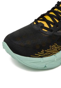 Crna tenisica za trčanje s teksturiranim gornjim dijelom, žutim naglascima i potplatom u boji metvice. Ima karbonsku ploču i istaknutu oznaku veličine.