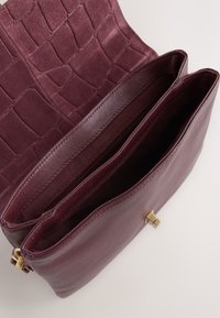 Burgundy leather bag with a textured croc pattern on the flap, featuring two compartments and a gold-tone closure. Smooth interior lining.