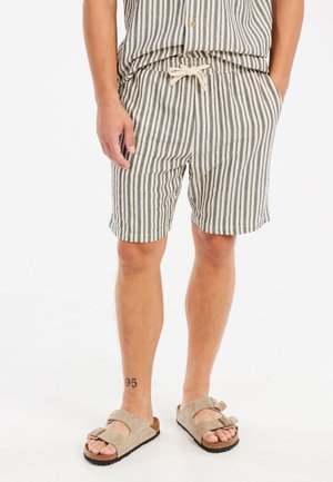 Gestreifte Shorts aus leichtem Stoff in Creme und dunklen Farben, mit elastischem Bund und Kordelzug. Getragen mit beigen Sandalen.