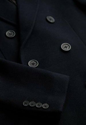 Blazer navy con design doppiopetto, bottoni neri e una texture in lana liscia, con quattro bottoni sul polsino della manica.