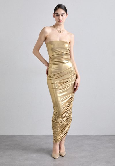 Rochie strapless metalică, aurie, cu un design strâns plisat, având o textură netedă și lucioasă și o siluetă până la podea. Complementată cu tocuri ascuțite.