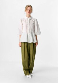 Weißes Blusenshirt mit Kragen und puffärmeln, mit einem Peplum-Taille; kombiniert mit lockeren, olivgrünen Hosen und weißen spitzen Schuhen.