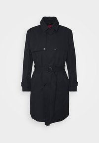 Trench-coat noir à double boutonnage avec ceinture à la taille, poignets boutonnés et col large sur fond uni.