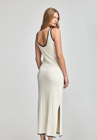 Knit ivory dress with ribbed texture, deep back, sleeveless design, and black trim accents. Features a side slit for added detail.