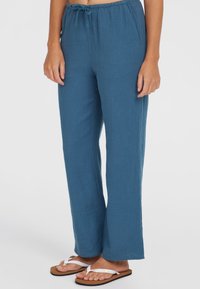 Lightweight, blue woven pants with a relaxed fit, elastic waistband, drawstring detail, and wide legs. Worn with white flip-flops.