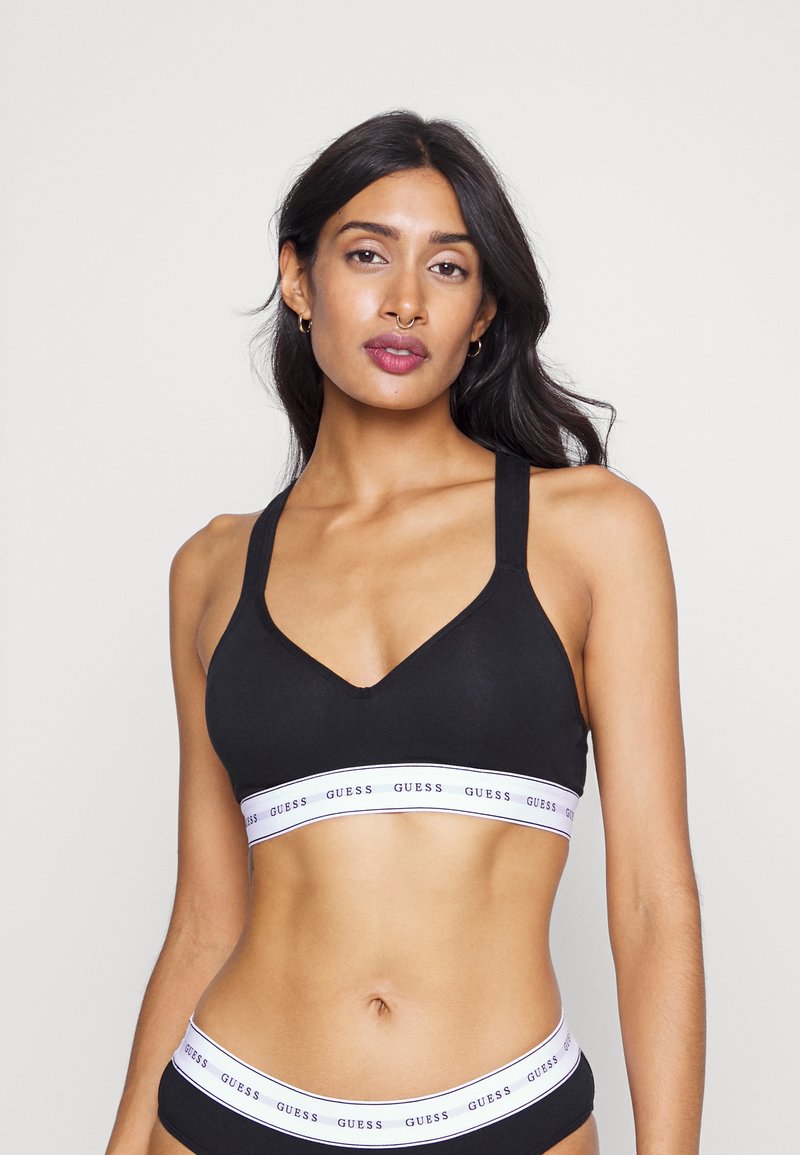 Svart bomulls-bralette med brede stropper og v-utskjæring. Har et hvitt bånd med "GUESS" i svart tekst langs bunnen.