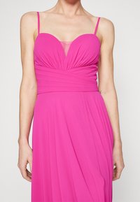 Robe plissée fuchsia avec un décolleté en cœur, des bretelles fines et des détails en maille transparente. Texture lisse et silhouette fluide.