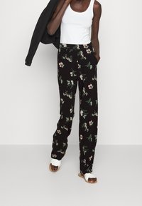 Black floral trousers with green leaves and pink flowers, loose fit, paired with a white tank top and white sandals.