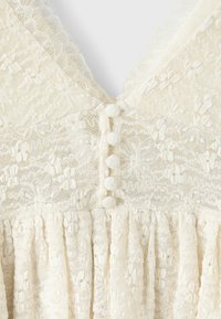 Corsage de robe en dentelle crème avec motifs floraux et boutons recouverts de tissu au centre devant.