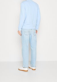 Sudadera de algodón azul claro de manga larga, combinada con jeans de mezclilla azul claro. Zapatillas blancas con suelas marrones visibles en la parte inferior.