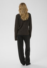 Brūns ribots adīts džemperis ar rotājumiem, kombinēts ar melnām plaša piegriezuma biksēm. Džemperim ir brīvs siluets un garas piedurknes.