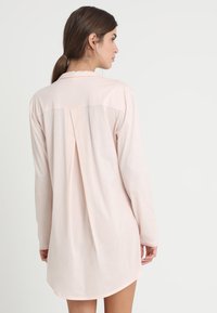 Abito camicia a maniche lunghe, di un delicato colore rosa chiaro, realizzato in tessuto morbido, con dettaglio di piega sul retro e orlo arrotondato per una vestibilità comoda.