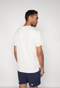 Λευκό κοντομάνικο μπλουζάκι με στρογγυλεμένο λαιμόκοψη, λεία υφή και άνετη εφαρμογή. Φοριέται με σκούρα μπλε σορτς με λευκές λεπτομέρειες.