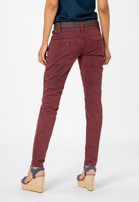 Maroon pants with a slim fit, featuring rear pockets and a textured black belt. Paired with tan wedge sandals with a patterned strap.