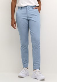 Ljusblå skräddarsydda byxor gjorda av ett slätt tyg, med slim fit, sidofickor och en platt frontdesign, i kombination med vita sneakers.
