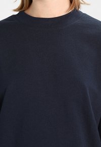 Sweat-shirt à col rond bleu marine en coton doux, doté d'une coupe décontractée et de coutures minimales. Texture lisse sans motifs visibles.