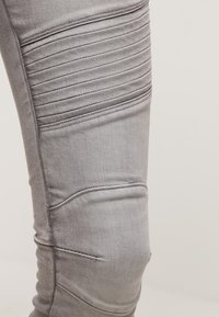 Pantalones de mezclilla gris con paneles texturizados en relieve en los muslos. La tela parece suave, con un ligero estiramiento y un diseño ajustado.