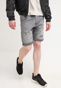 Shorts de mezclilla gris con bordes deshilachados y detalles desgastados, combinados con zapatillas negras. El conjunto presenta un ajuste casual y relajado.