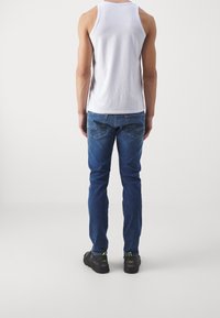 Jeans de mezclilla azul con un corte ajustado, que cuentan con bolsillos traseros con detalles de costura, combinados con una camiseta de tirantes blanca lisa y zapatillas negras.