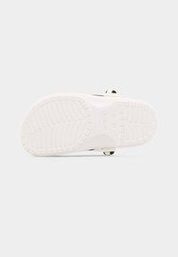 Σόλα από λευκό παπούτσι Crocs με μαύρο και λευκό λουρί, μέγεθος 11, διακριτό μοτίβο πέλματος σε απλό ανοιχτό φόντο.